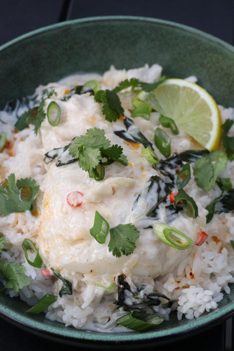 Bowl filled with white jasmine rice topped with Thai-Inspired Coconut Lemongrass Poached Fish. The fish is garnished with cilantro and a lime wedge.