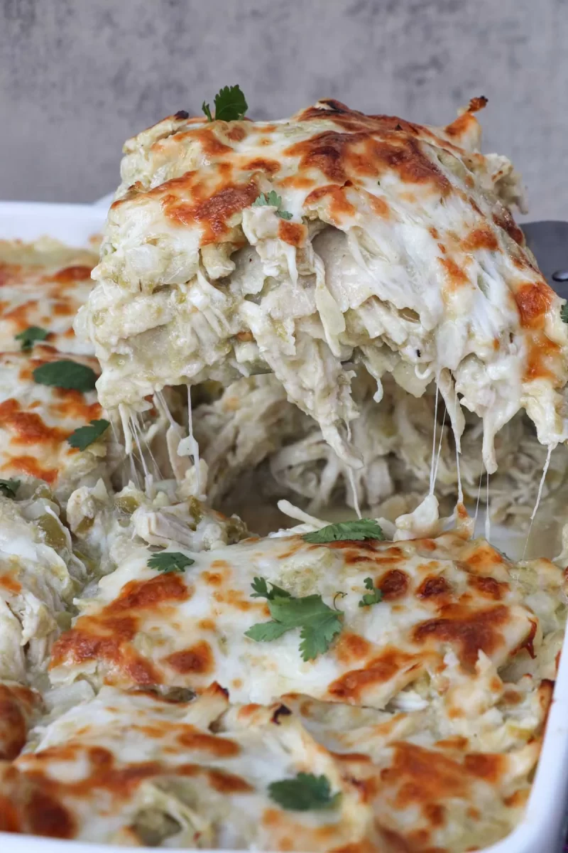 A gooey, cheesy serving of Chicken Enchilada Casserole is being lifted from the casserole dish.