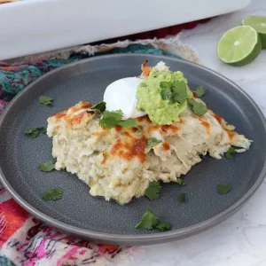 Plate with a single serving of Chicken Enchilada Casserole, topped with sour cream, guacamole, and cilantro.